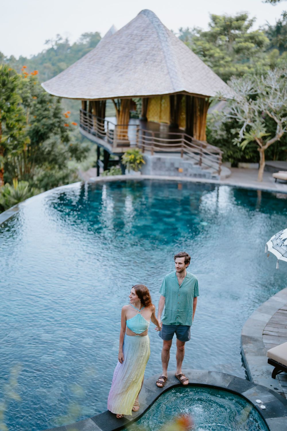 Luxury infinity pool overlooking tropical mountain landscape with thatched roof villas.