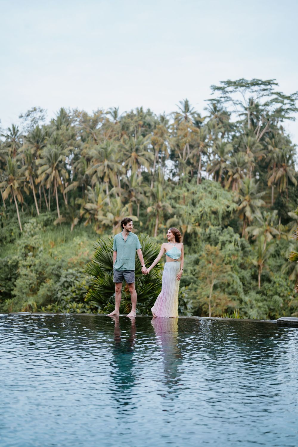 Couple enjoying sunset at an infinity pool surrounded by lush palm trees in Bali.