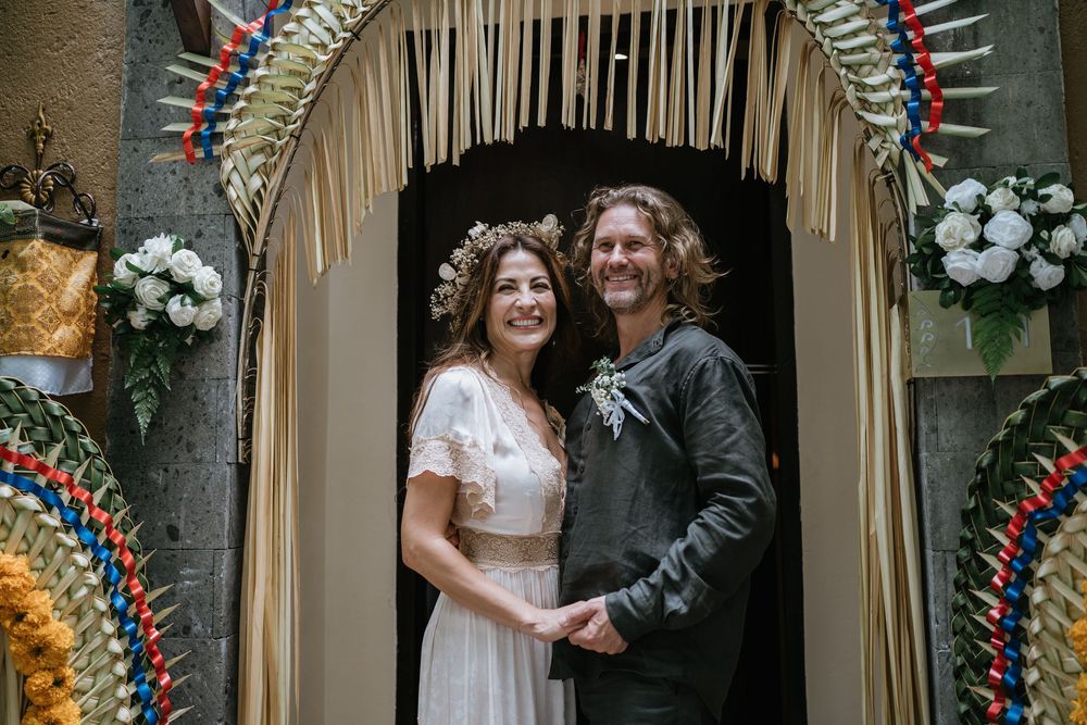 Wedding couple poses under decorated archway with floral arrangements.