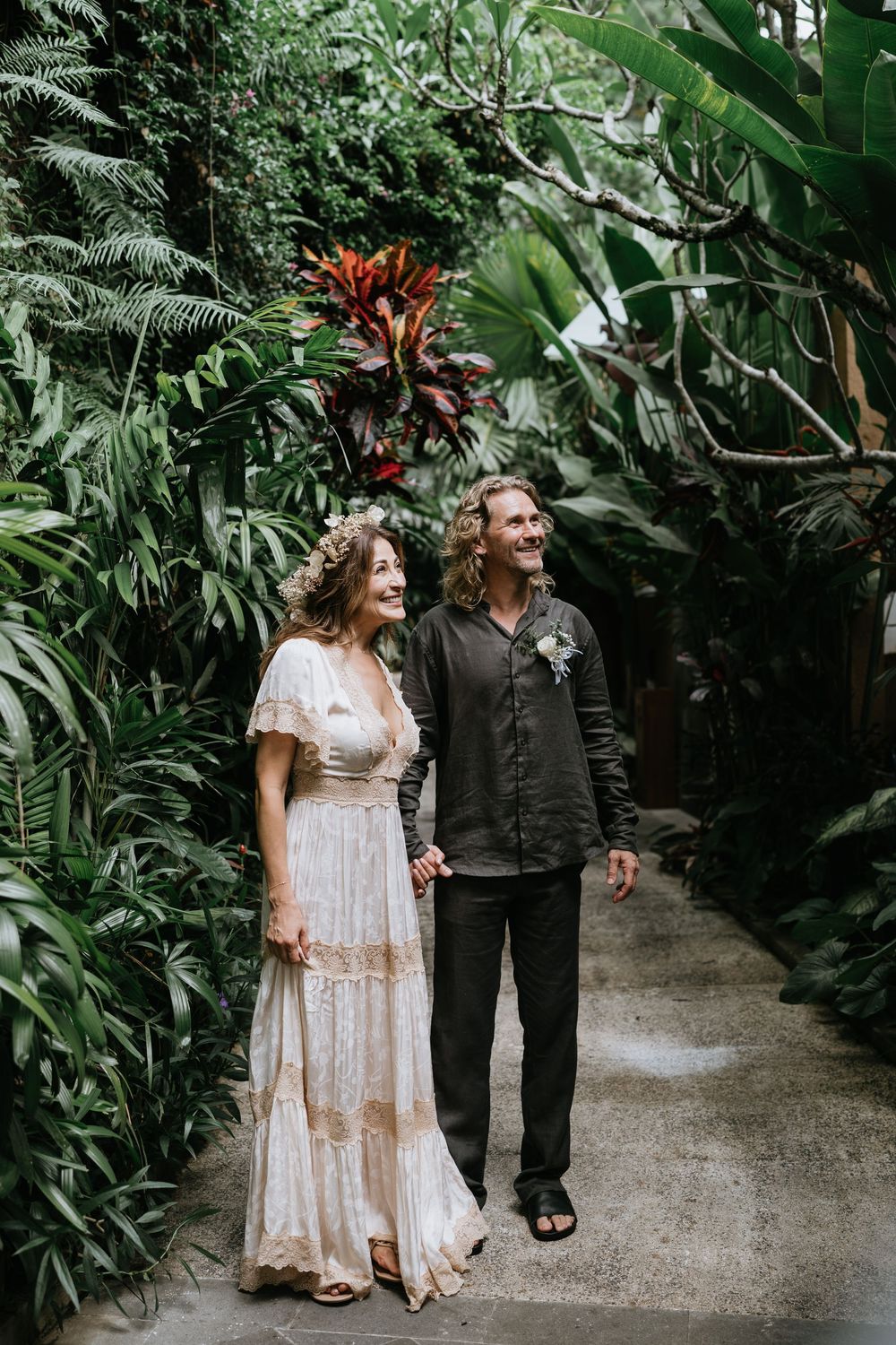 Couple walks hand in hand through lush tropical garden pathway.