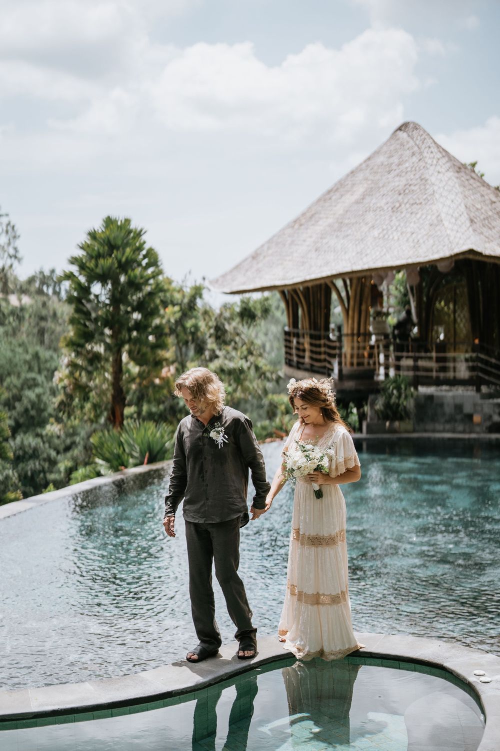 A couple stands on a wooden platform overlooking a serene pool at a tropical resort.