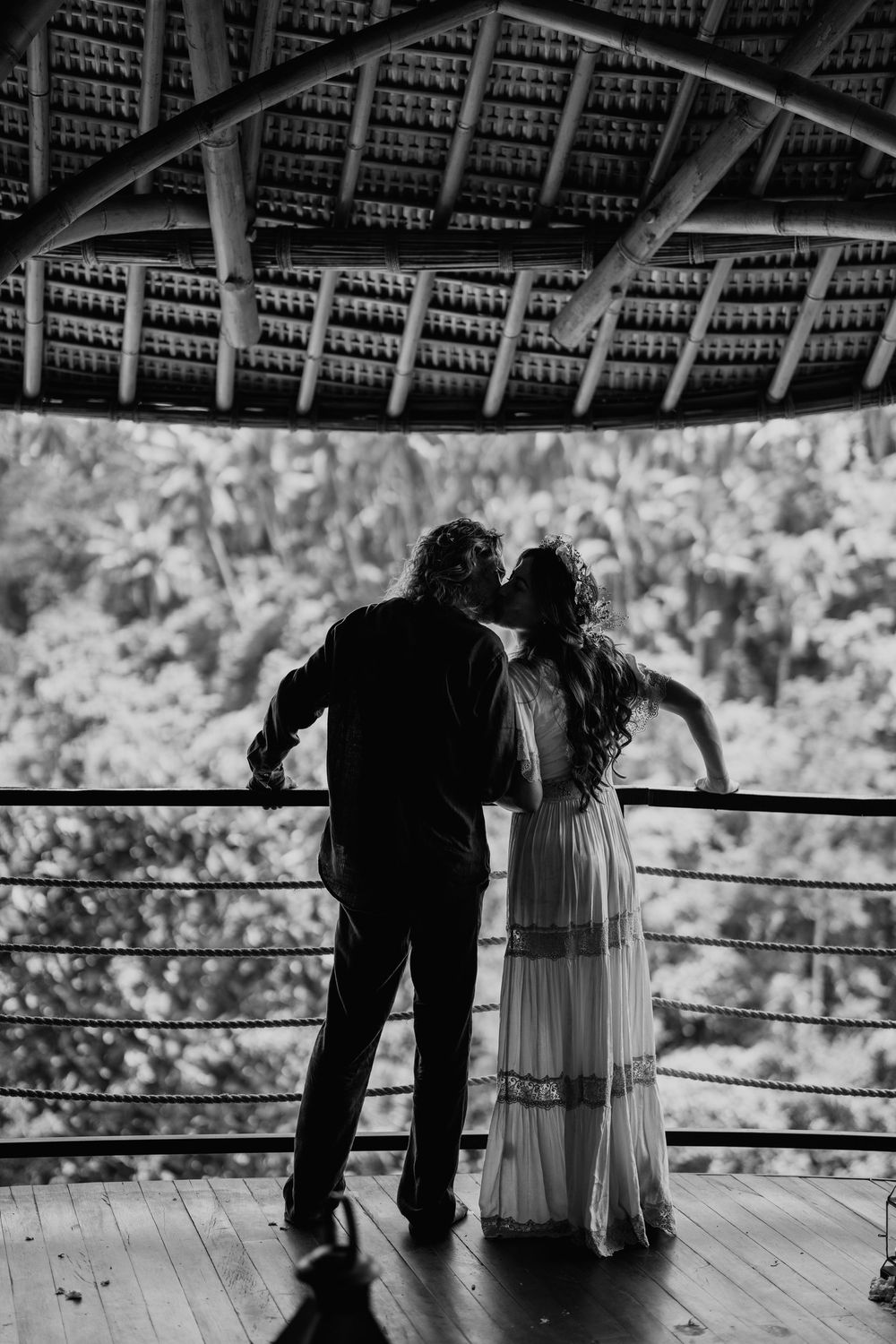 Silhouettes of a couple standing on a covered deck against a bright background.