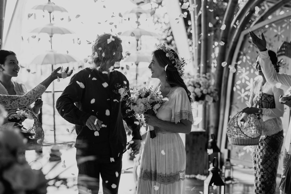 Wedding celebration captured in black and white under a traditional thatched roof structure.