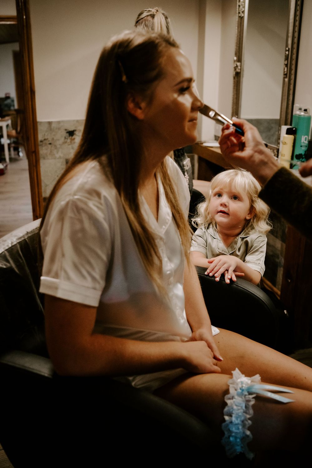 Behind the scenes preparation shows makeup application in progress while a small child watches with curiosity.