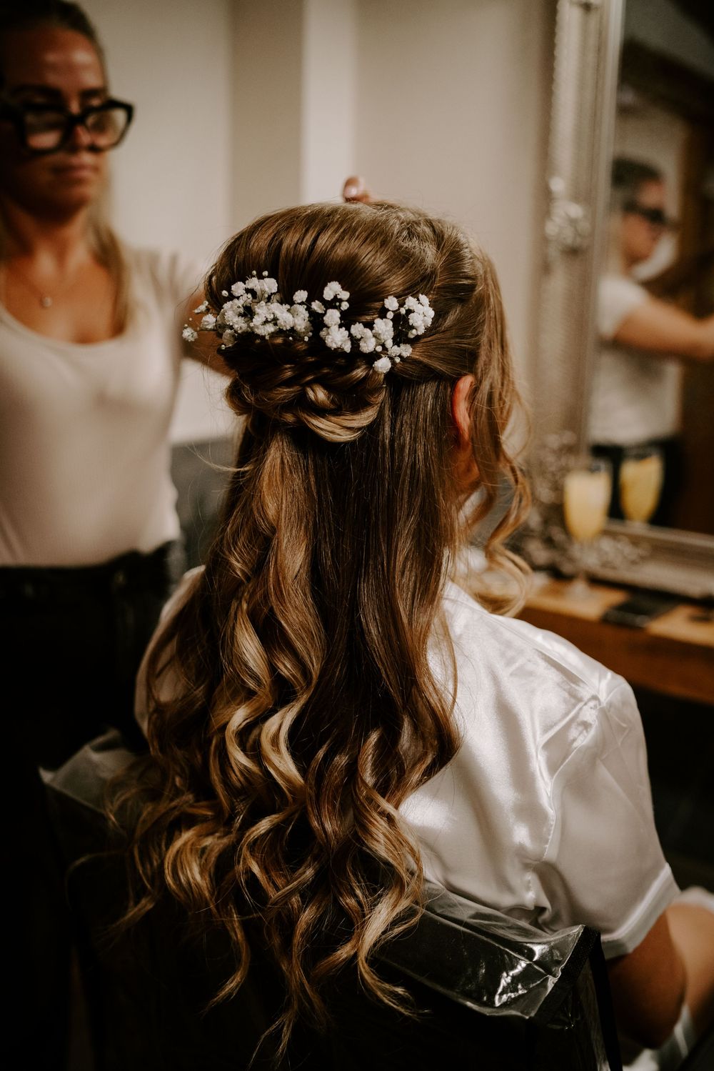 Elegant bridal hairstyle featuring long wavy curls adorned with delicate white floral hairpiece.