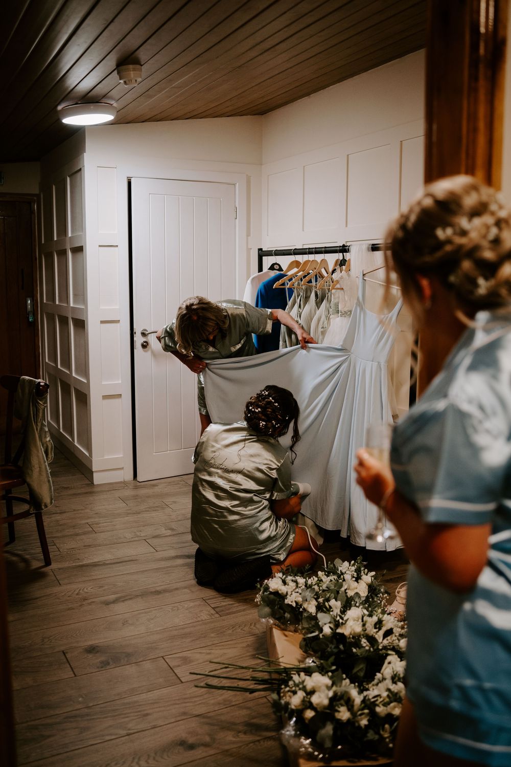 Getting ready in a rustic wood-paneled room with floral arrangements and hanging garments.