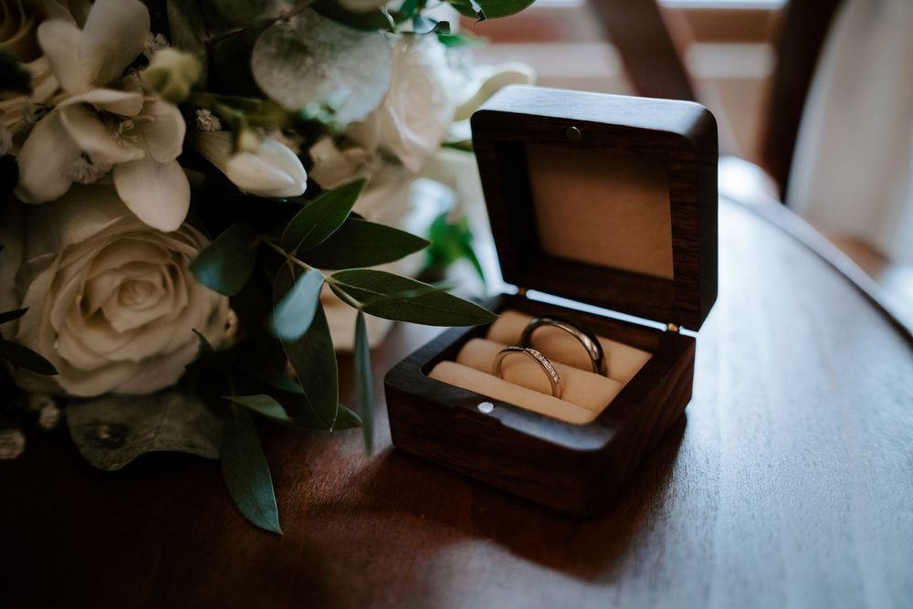 Wedding details including white roses, jewelry box, and delicate floral arrangements on a wooden surface.