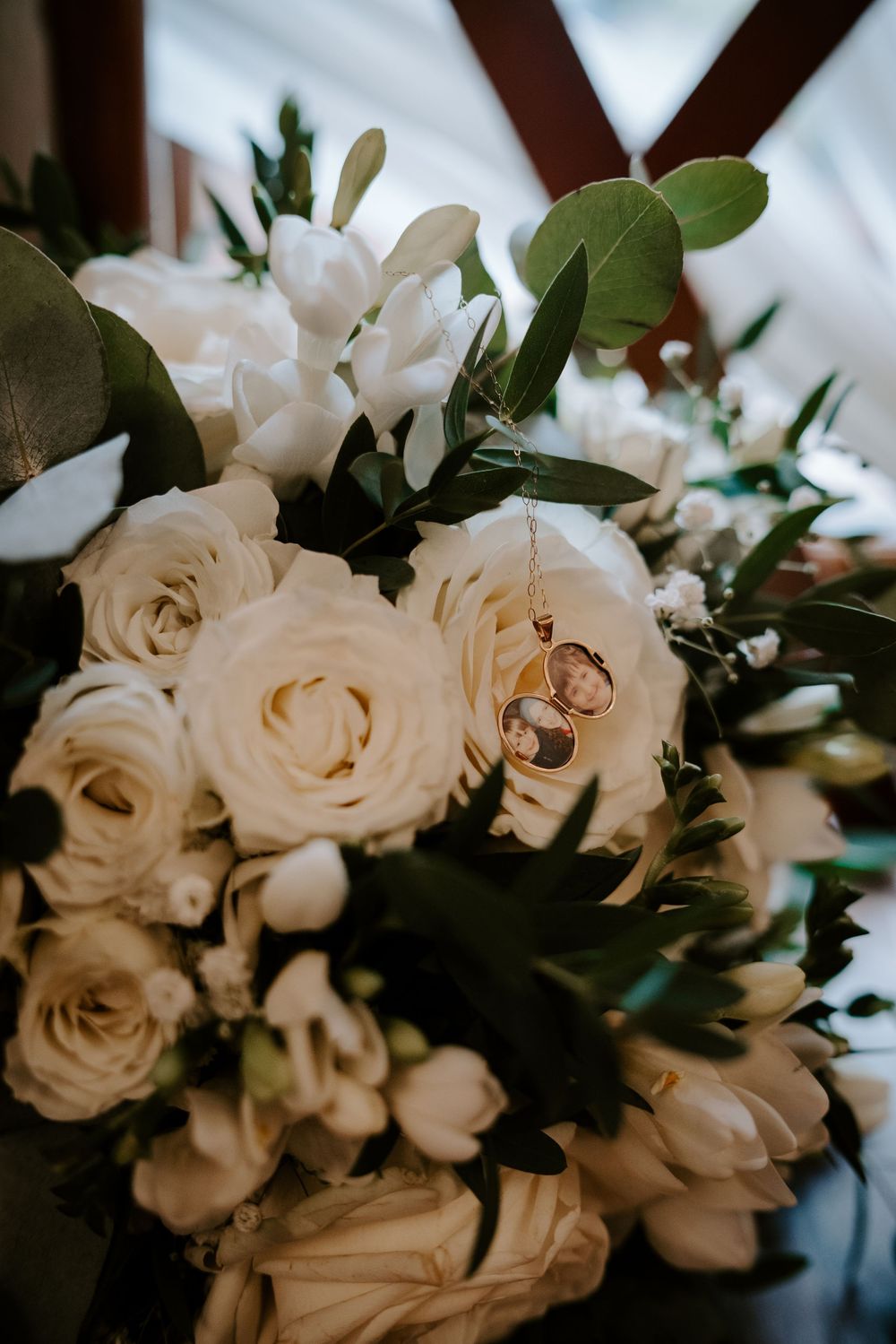 White roses and wedding rings arranged in an elegant bridal bouquet with green foliage.