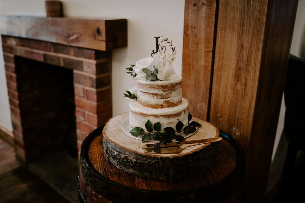 Wedding cake details with white frosting displayed on rustic wooden barrel decorated with greenery and floral accents.