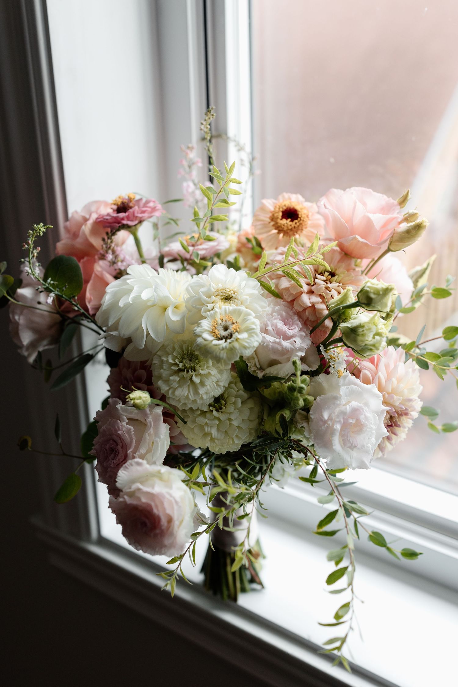 A romantic arrangement of pink and white peonies with greenery sits elegantly on a bright windowsill.