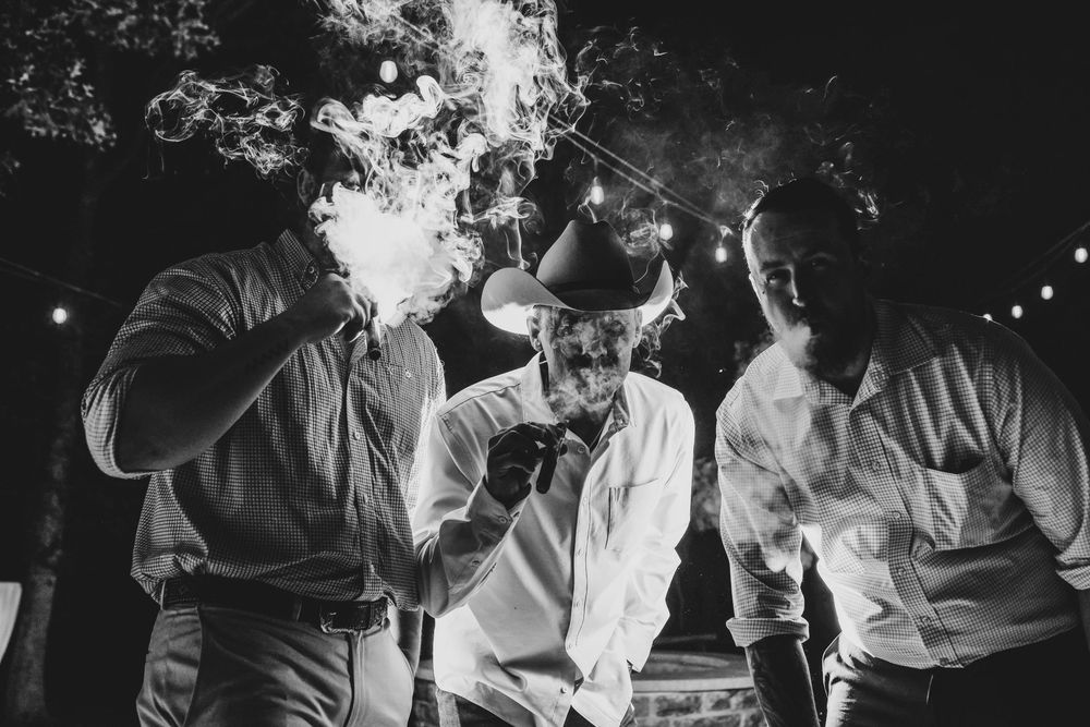 Groom and groomsmen enjoying a cigar bar with cowboy hats and rustic wedding style