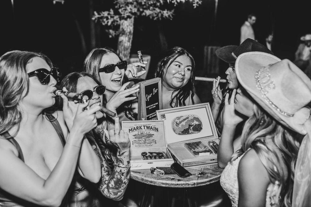 fun upbeat vibes of bride and her bridesmaids smoking cigars at the reception