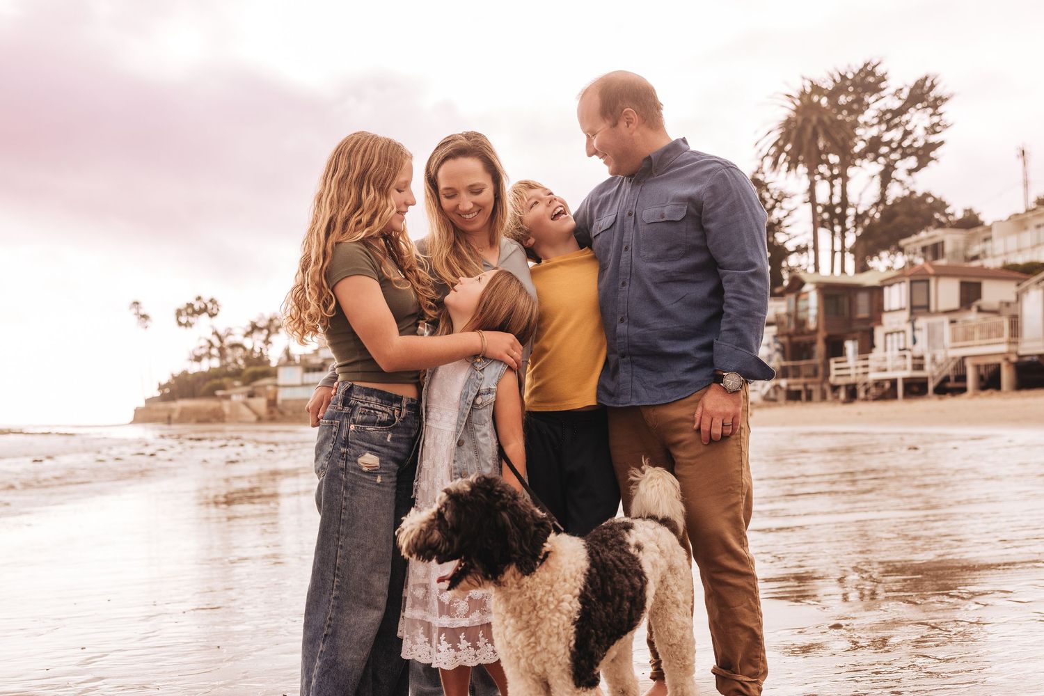 A family stands with their dog in front of rustic gray wooden doors covered in climbing vines on a stone wall.