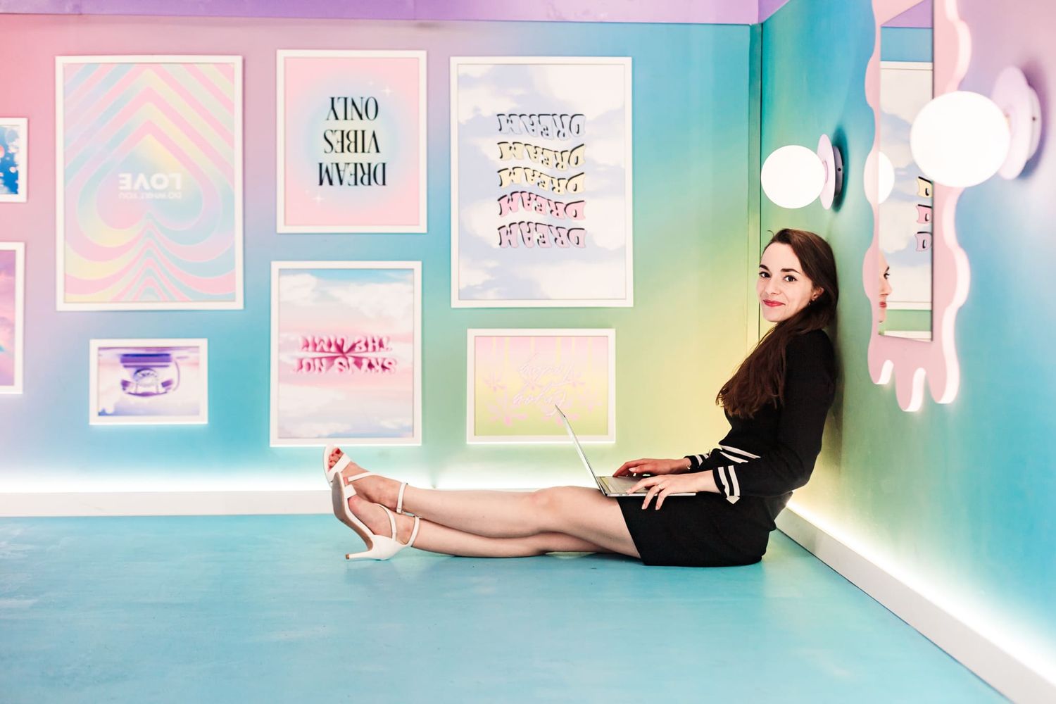 Young woman sitting on floor with laptop in colorful pastel room with art prints.
