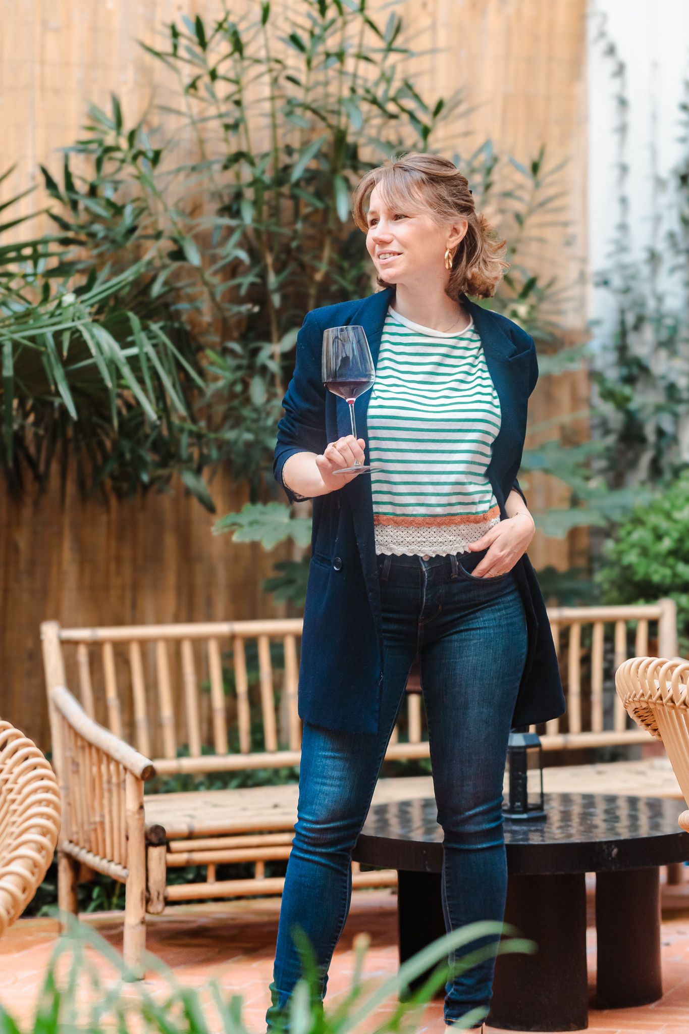 Woman holding a glass of red wine standing in a tropical outdoor patio setting.