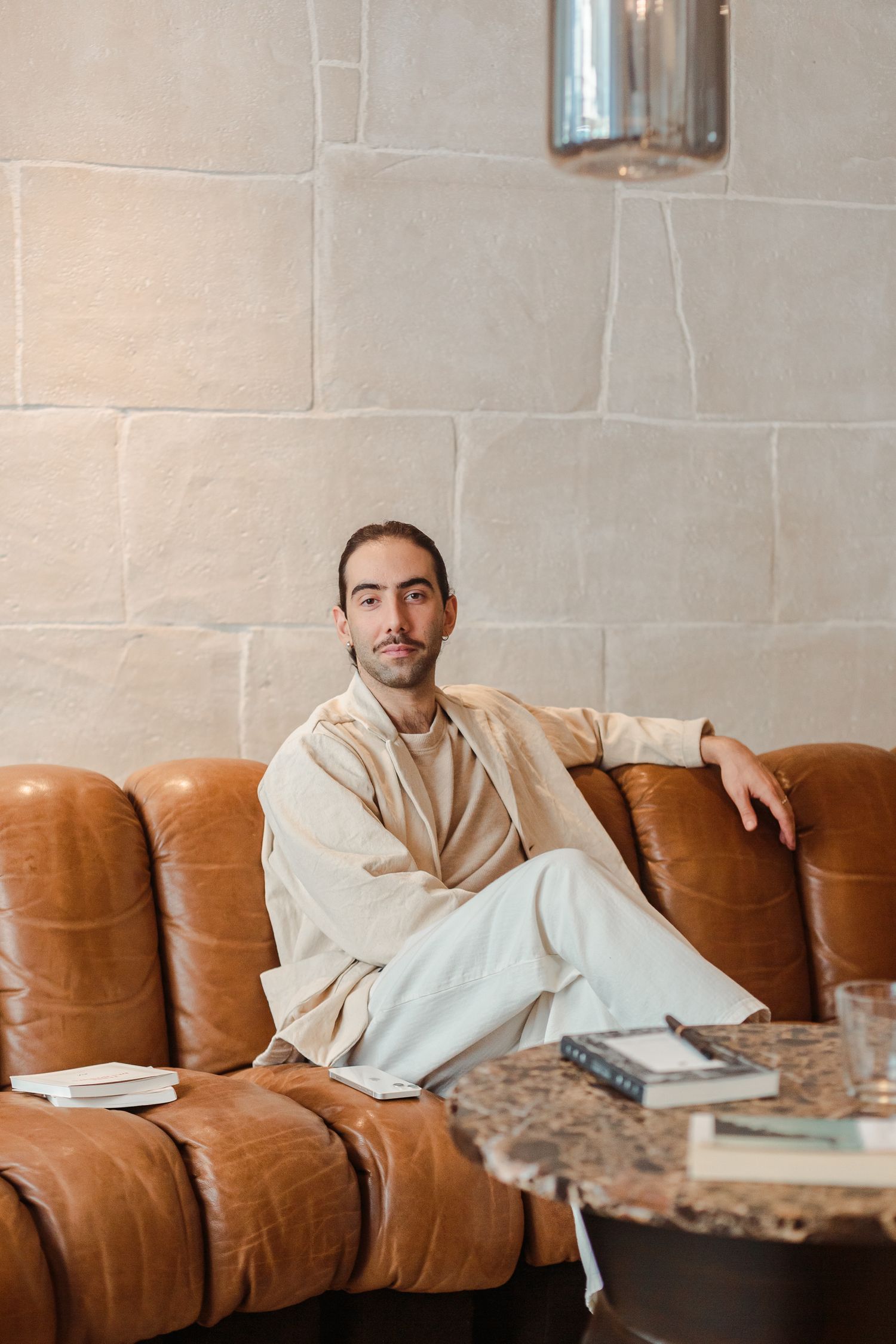 Stylish man in beige outfit sitting relaxed on a brown leather sofa in a luxury interior.