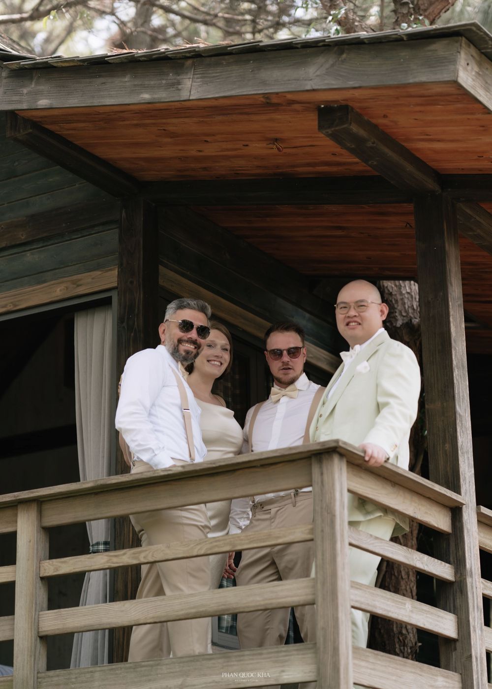 Groom in a light green suit posing with groomsmen on a wooden balcony surrounded by trees on the wedding day.
