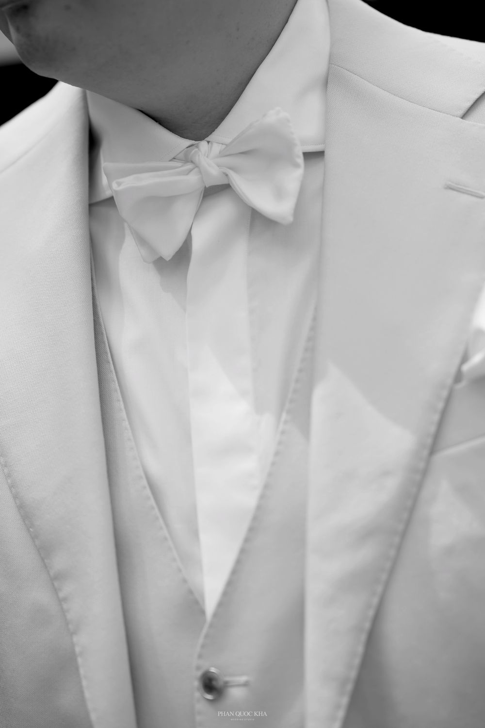 Close-up black and white detail of grooms ivory suit with white bow tie and vest.