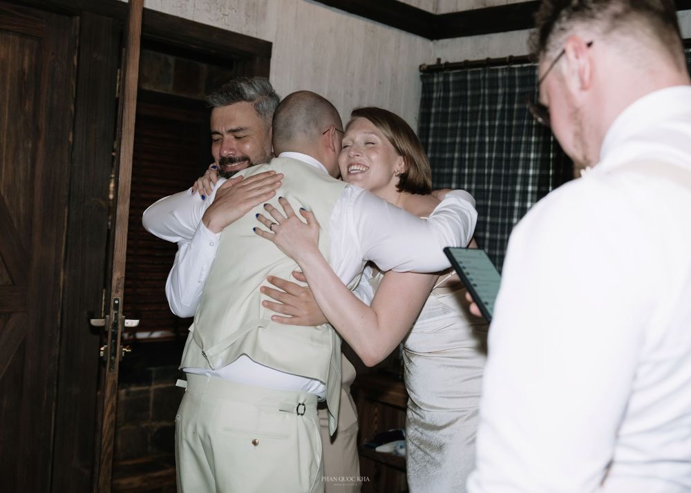 Joyful bride in white dress hugs groom while groomsmen celebrate at wedding venue.