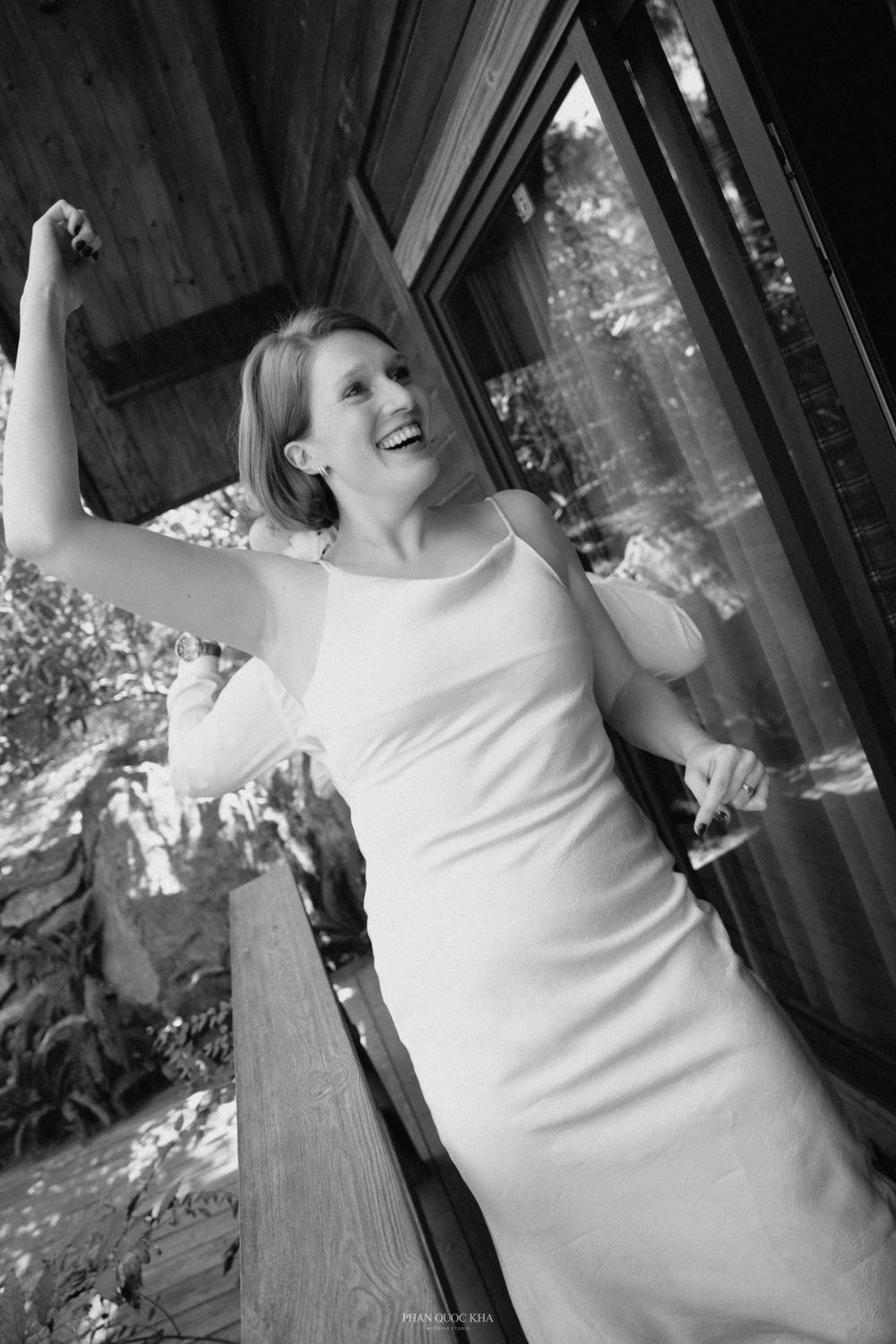 Black and white photo of laughing bride in sleek white gown on rustic wooden deck.