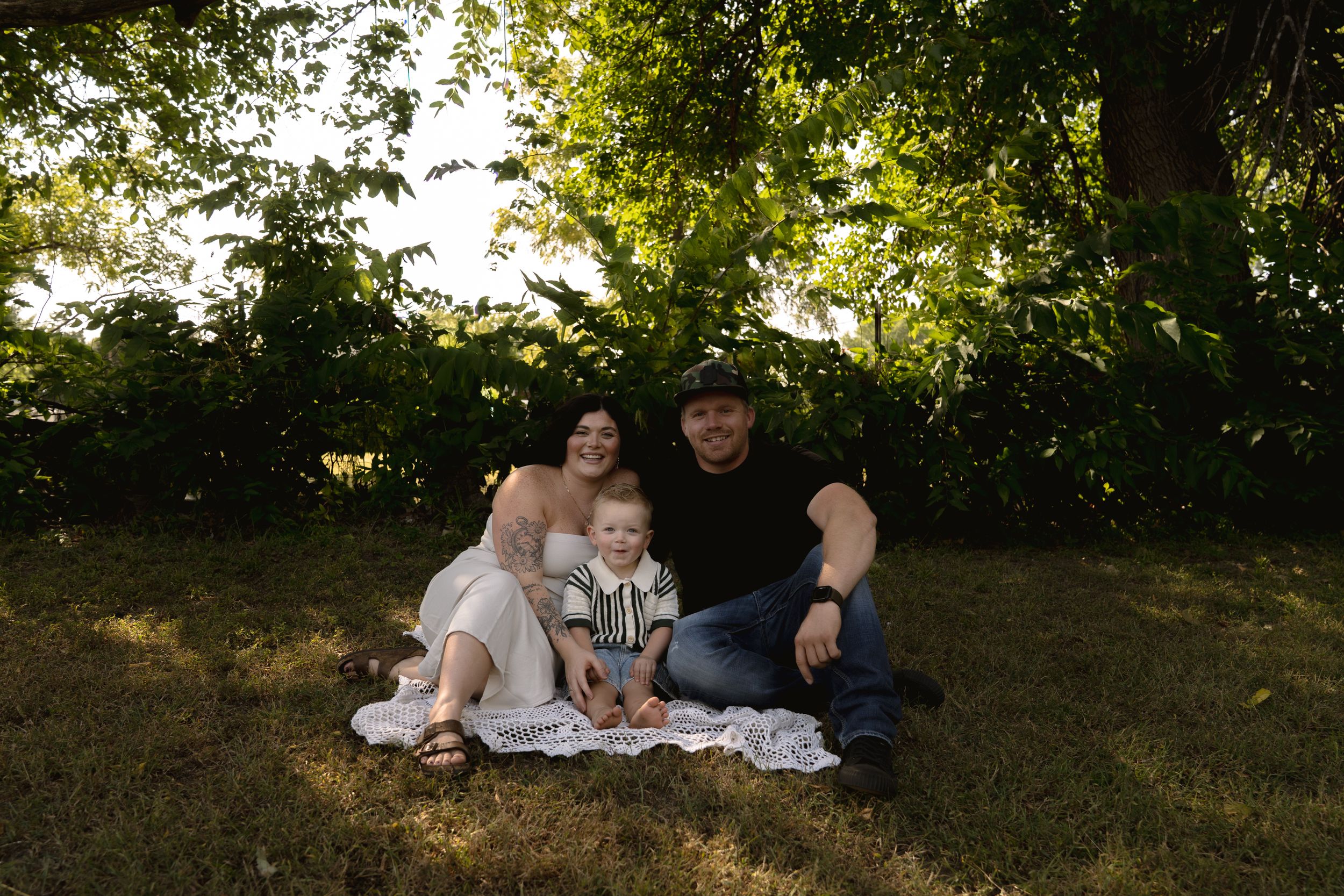 Family relaxing together on a grassy hill during golden hour with trees in the background.