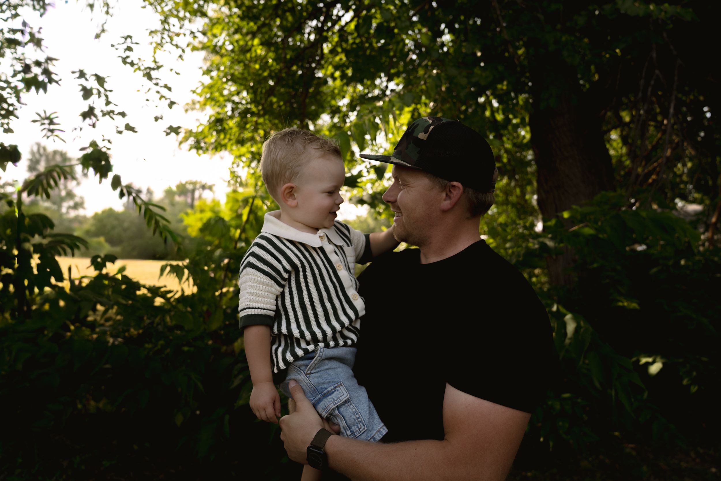 Outdoor family photoshoot under tree canopy with warm evening light filtering through.