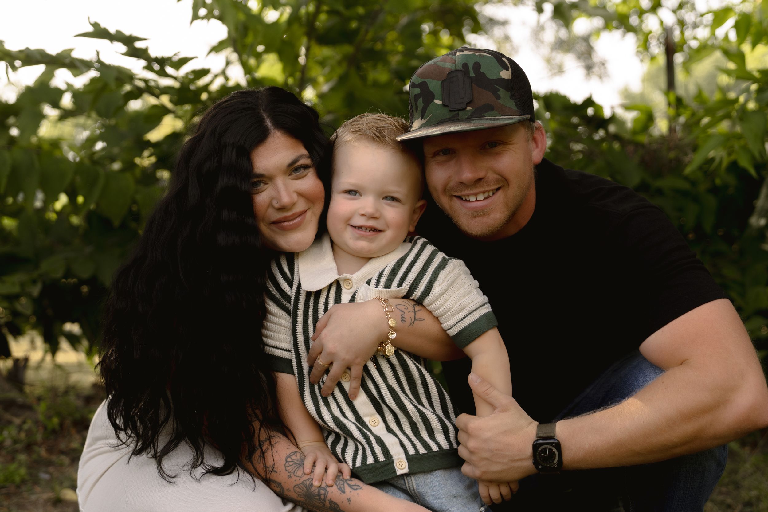 Candid family moment captured under trees during an outdoor photo session.