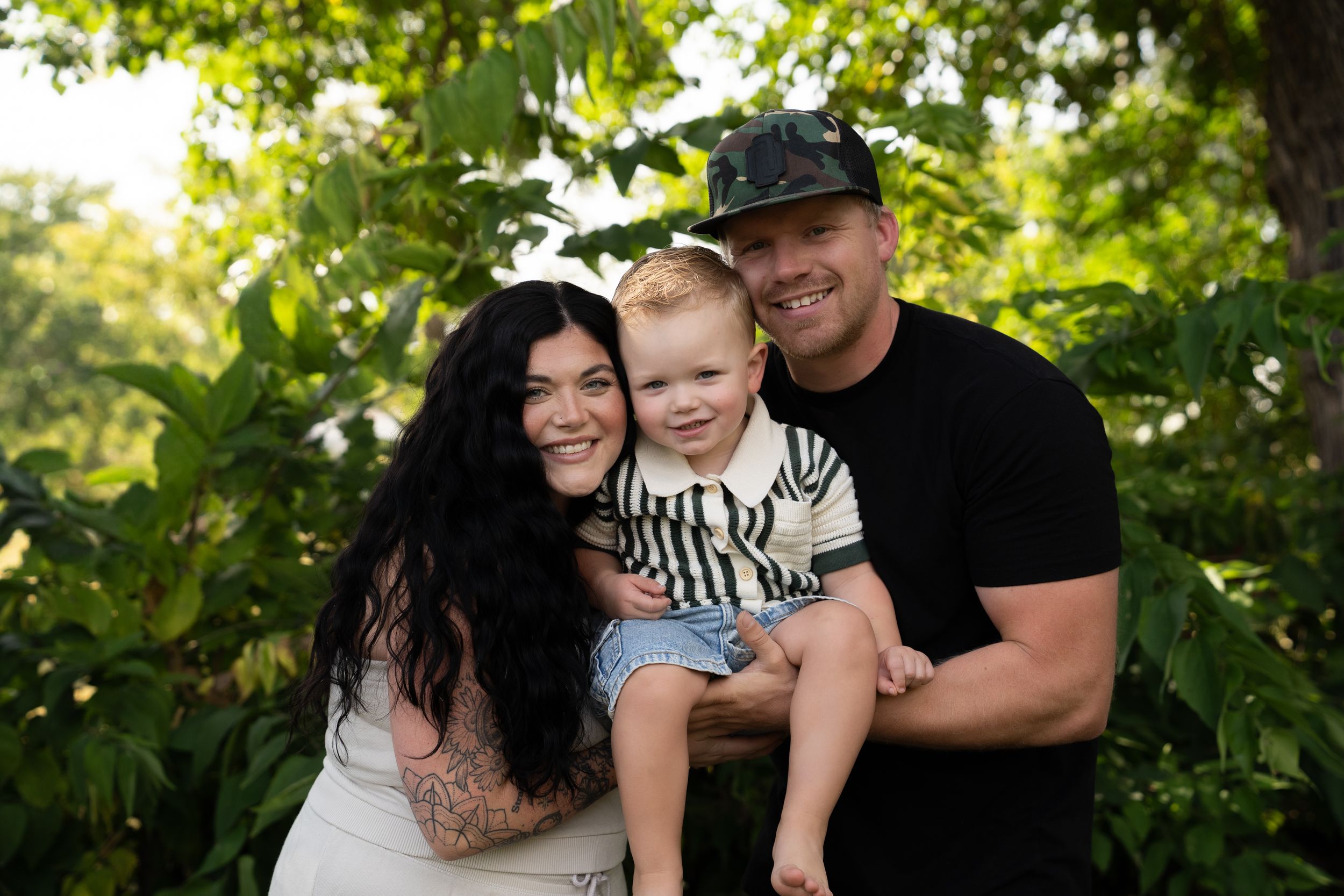 Family embracing during a casual outdoor photoshoot with green foliage backdrop.