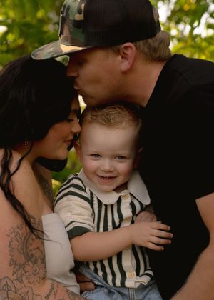 A joyful toddler in a striped shirt smiles while being embraced in a loving family moment outdoors.