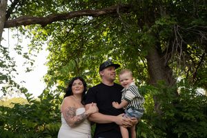 A family poses together under a leafy green tree during an outdoor photo session.