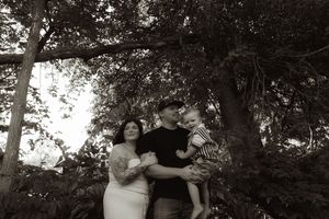A black and white portrait of a family embracing under tall trees.