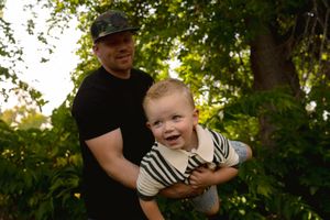 A playful moment captured between a toddler in stripes and an adult in a black shirt outdoors.
