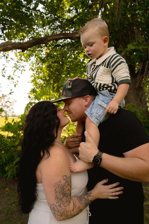 A tender family moment captured outdoors with a toddler in striped shirt and denim shorts.