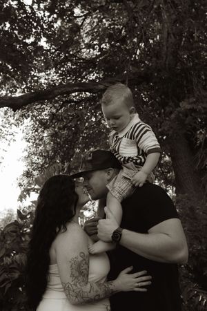 An intimate black and white family portrait taken under a canopy of trees.