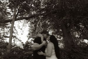 A black and white portrait of a tender family embrace under tree branches.
