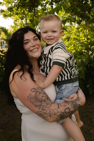 A heartwarming portrait of a toddler in striped shirt with tattooed arms holding them.