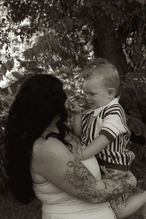 A black and white intimate moment between a tattooed person and child in striped shirt.