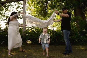 Family plays with delicate lace fabric outdoors as child stands beneath.