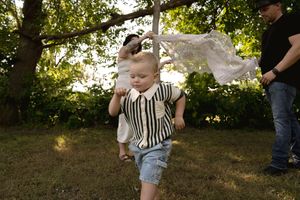 A small child in a striped shirt plays under a lace canopy held up in a backyard setting.