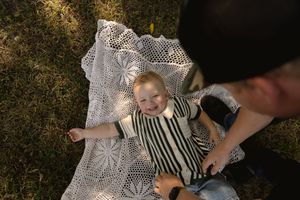 Child lies on decorative lace blanket during outdoor photo session.