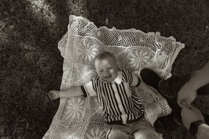 Black and white photo of child on vintage lace blanket outdoors.