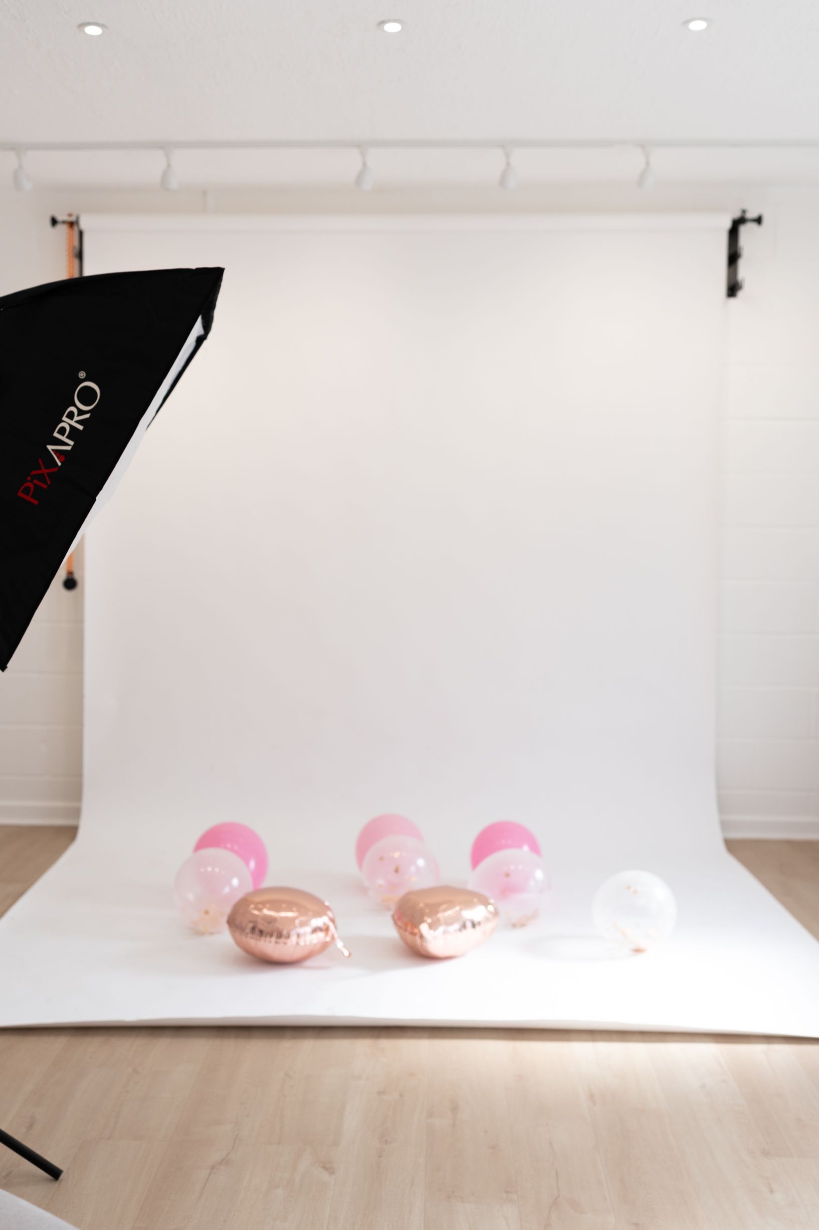 A minimalist birthday photography setup with pink balloons arranged against a white background in a studio in Cambridge, UK