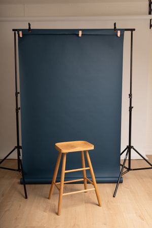 Professional studio photography headshots setup showing a navy blue backdrop roll and wooden stool. Cambridge, UK