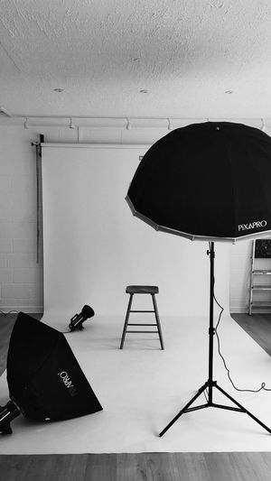Professional photography studio space with white backdrop, lighting equipment, stands, and black umbrellas ready for setup in Cambridge, UK