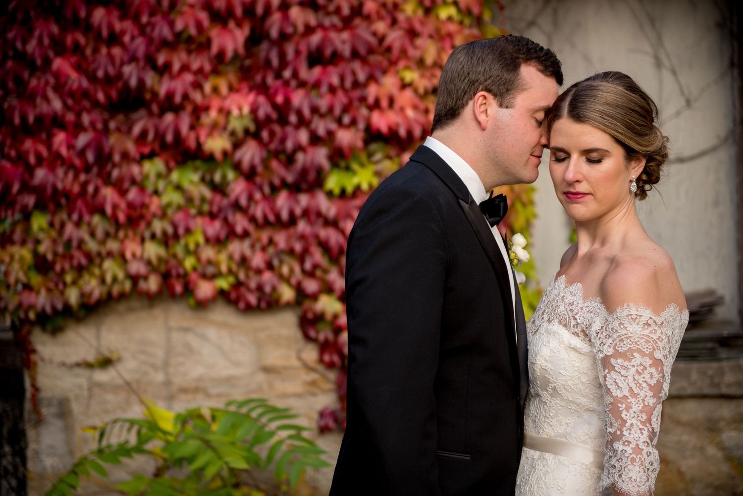 A romantic fall wedding photo shoot against a backdrop of vibrant red autumn ivy on stone walls.