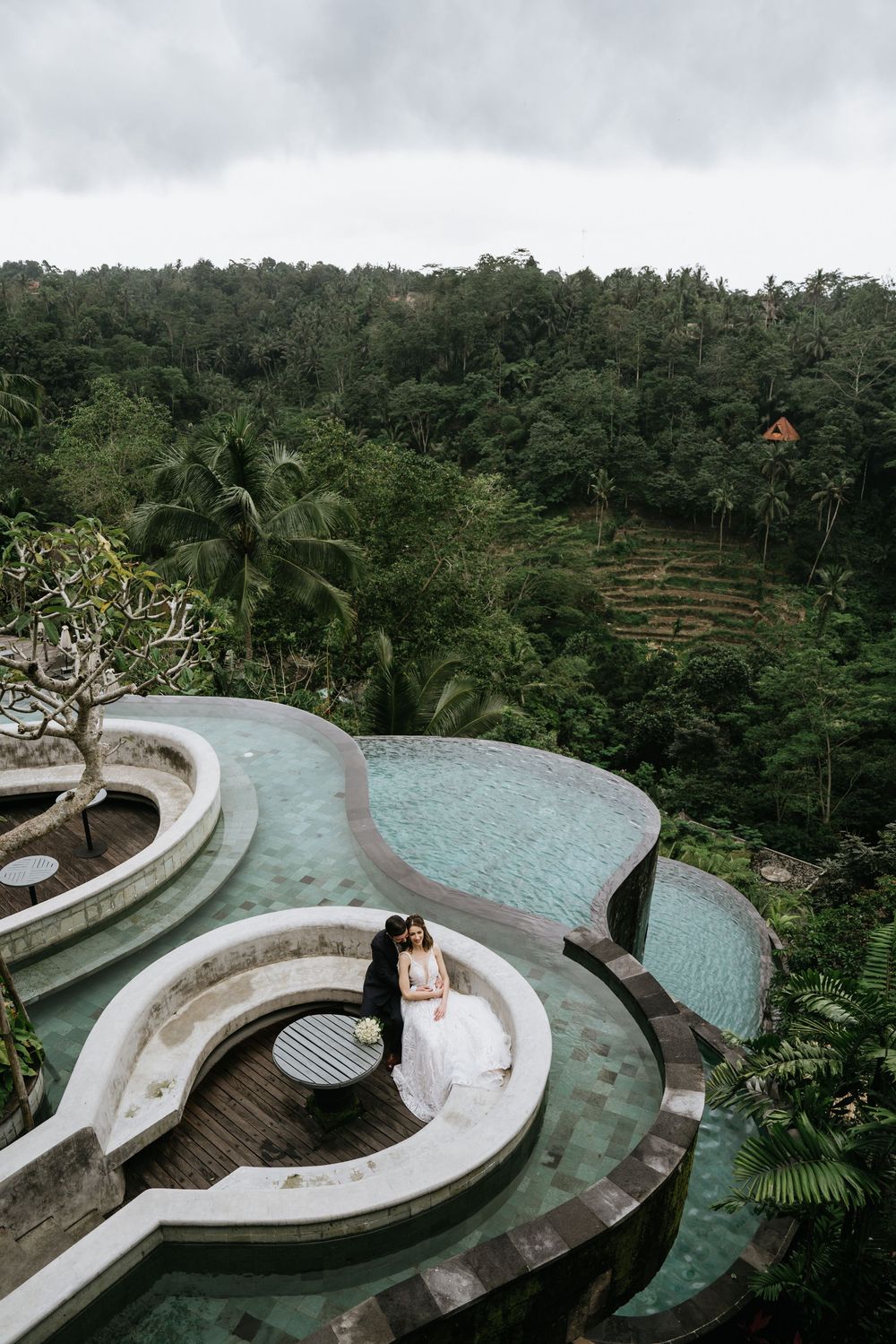 A luxurious infinity pool with curved edges overlooks a lush tropical forest landscape in Bali.