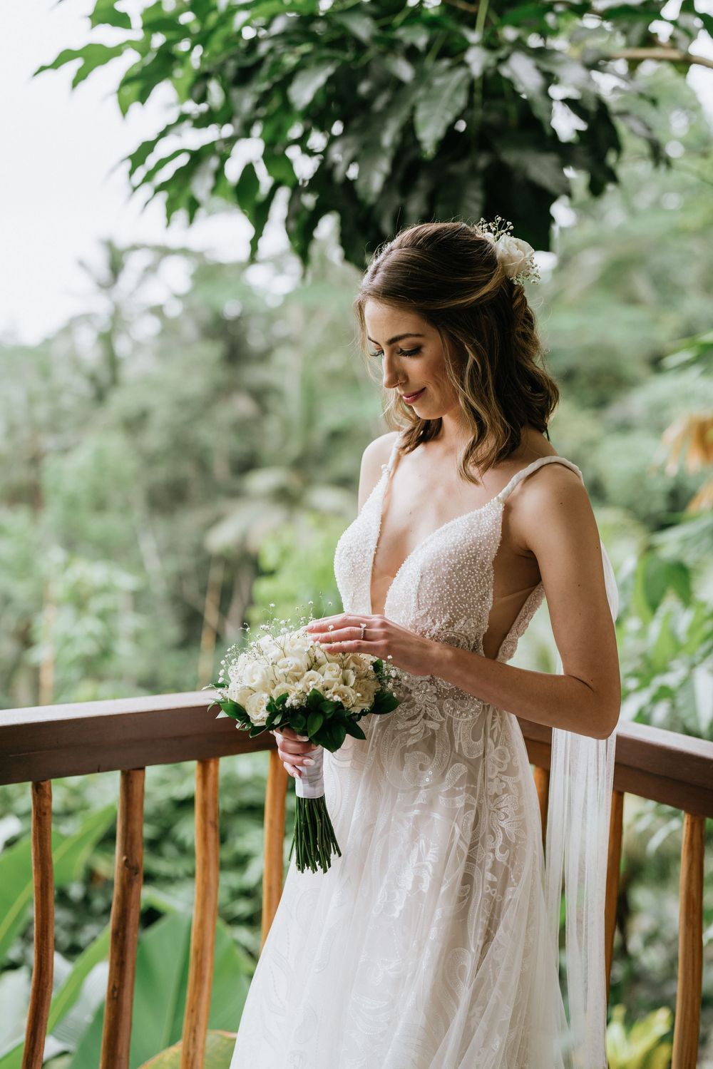 Elegant lace wedding dress with delicate details photographed on a balcony with green foliage.