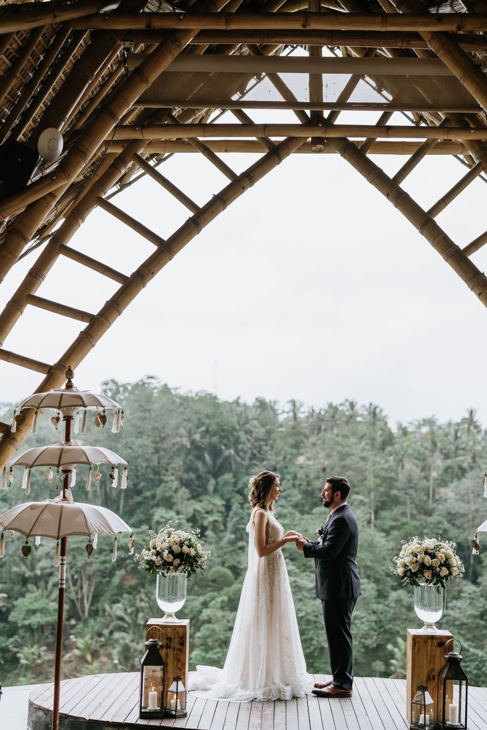 Elegant tropical wedding venue with wooden beams and hanging lanterns overlooking palm trees.