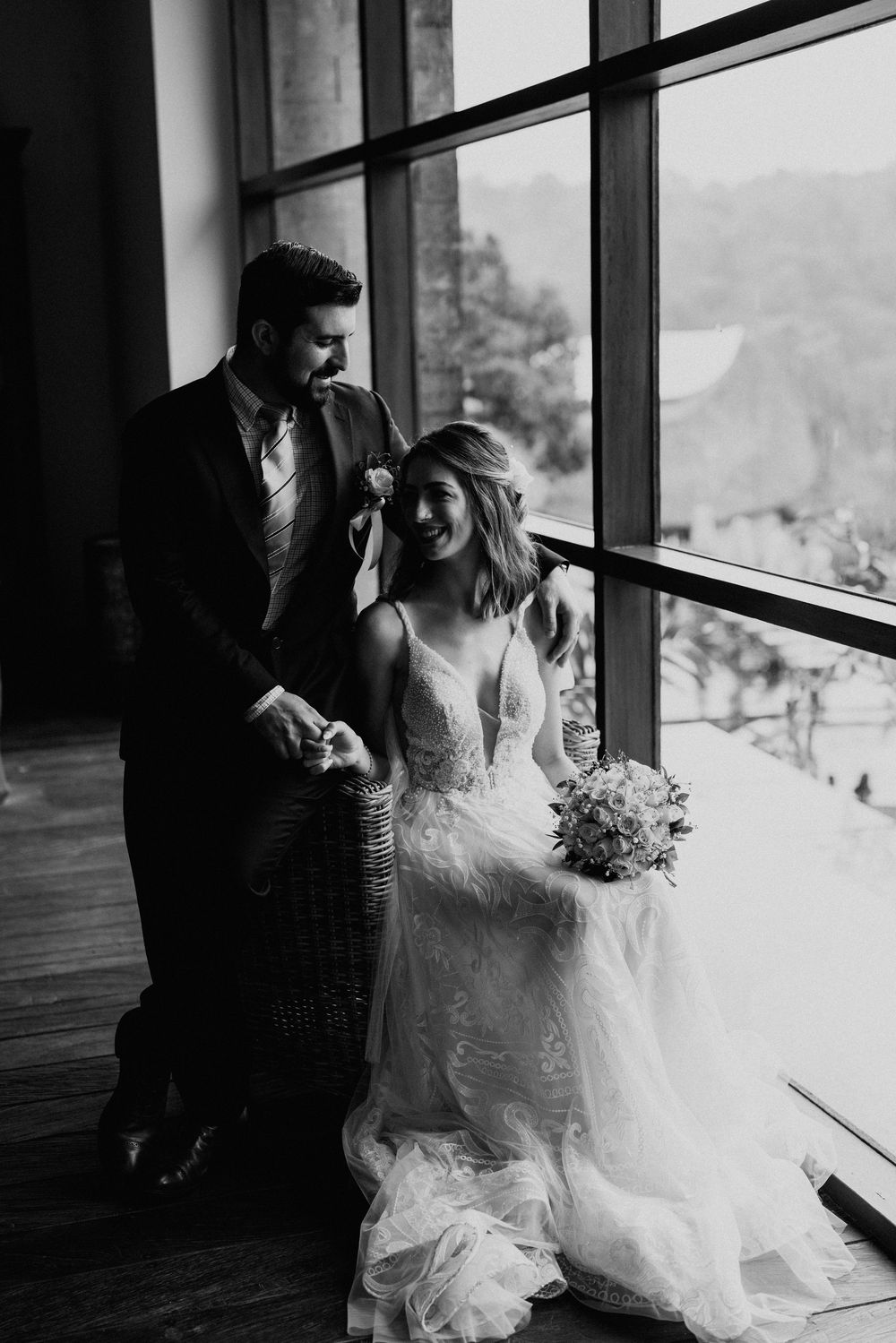 Black and white photo of newlyweds sitting by floor-to-ceiling windows with mountain views.