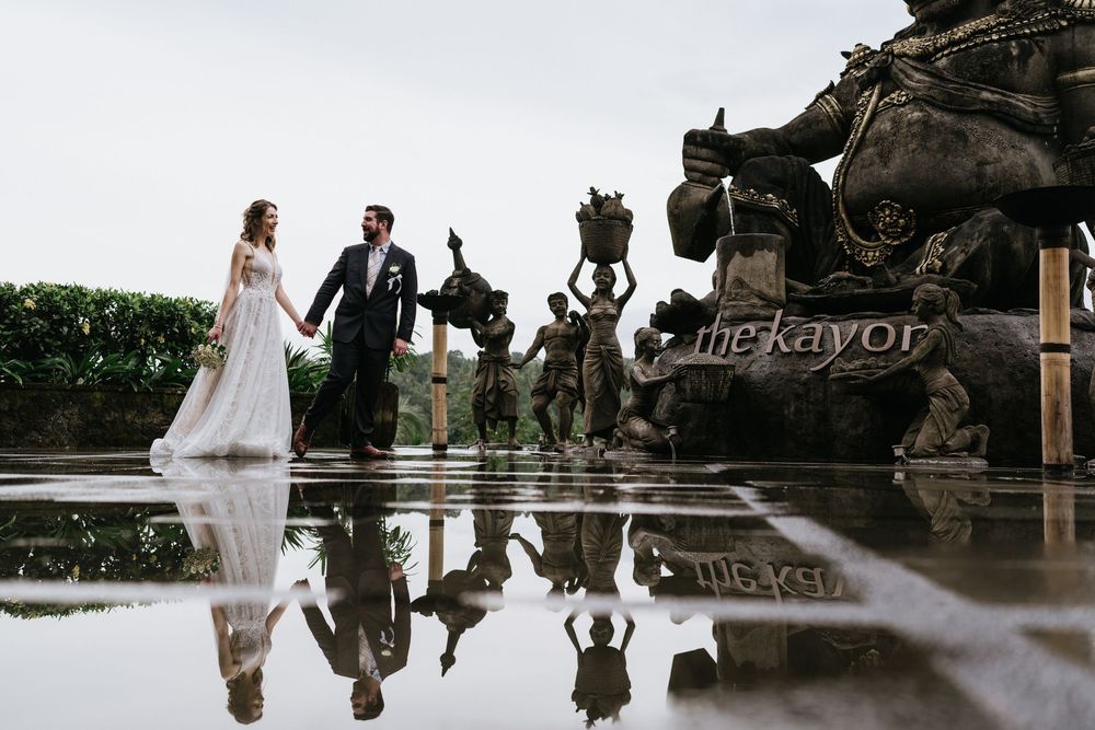 Artistic reflection shot of wedding couple in puddle at outdoor venue.